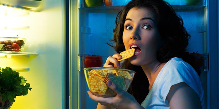 Девушка ест крекеры перед открытым холодильником